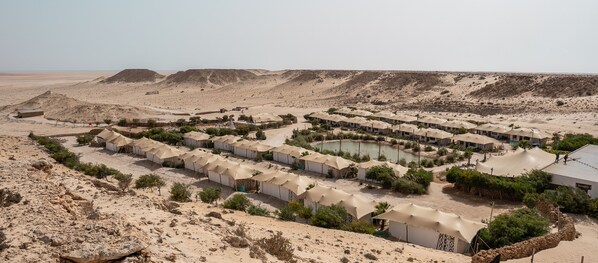 A desert resort with multiple tents, a central pool, and sparse vegetation.