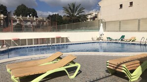 A swimming pool with lounge chairs, a lifeguard stand, and a fenced area with a view of residential buildings.
