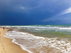 Una platja amb onades, un cel clar i algunes persones passejant.