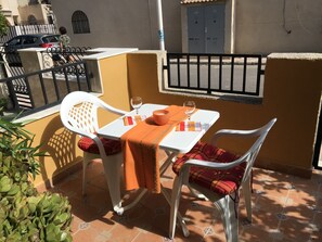 A small outdoor patio with a white table and two white chairs, one with a plaid cushion.