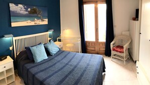 A bedroom with a bed, bedside tables, a lamp, a chair, and a painting of a beach scene.