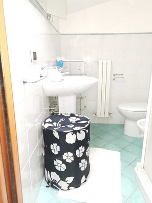 A bathroom with a white sink, toilet, and a round trash bin with a floral cover. - Attico Marina (Roseto degli Abruzzi)