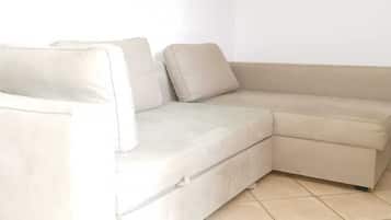 A beige sectional sofa with a curved design, positioned in a room with white walls and tiled flooring.