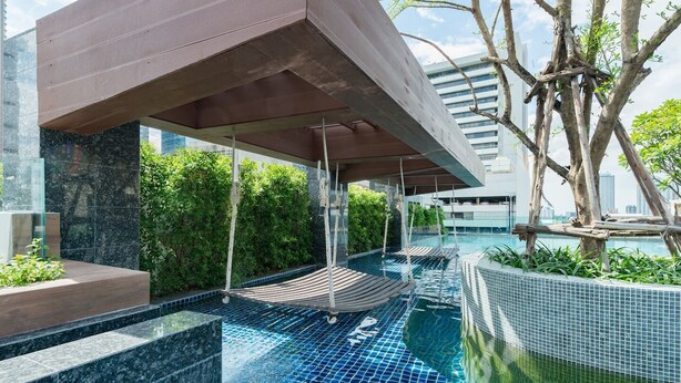 Un área de piscina exterior moderna con cerramiento de vidrio, tumbonas de madera y vistas al horizonte de la ciudad.