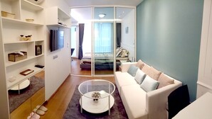 Una habitación de hotel moderna con un sofá blanco, una mesa de centro de vidrio y una cama con colcha a rayas.