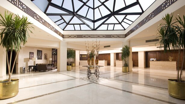 A spacious lobby with a high ceiling, a central decorative fountain, and multiple reception desks. - Eagle's Paradise Beach Resort Abu Soma (Safaga)