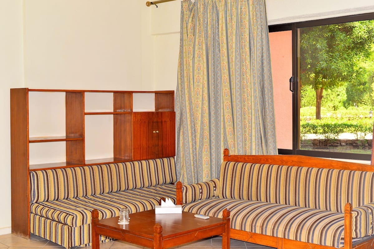 A room with a wooden bench and a sofa, a small table with a tissue box, and a window with a view of greenery.