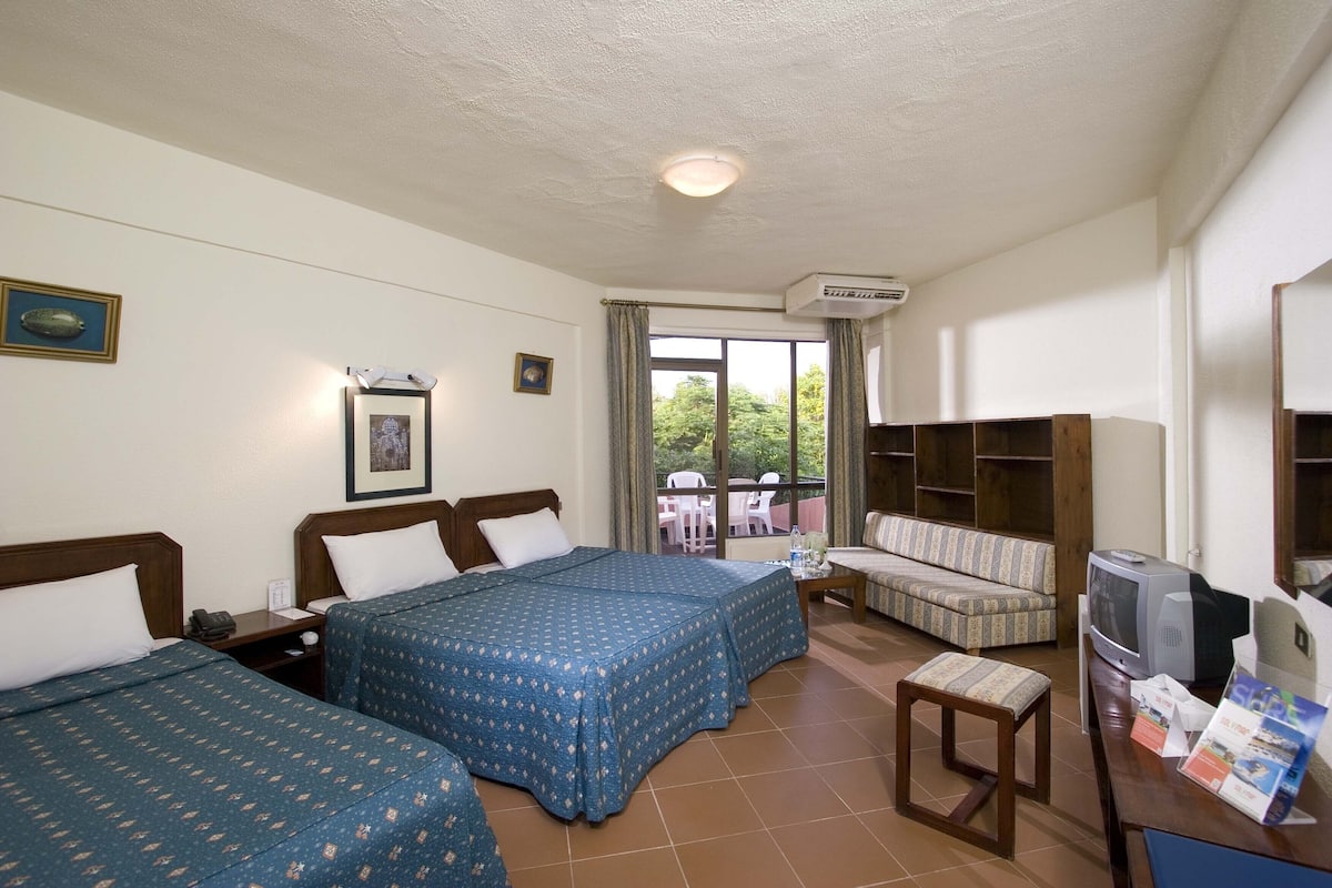 A hotel room with two beds, a sofa, a television, and a small table.