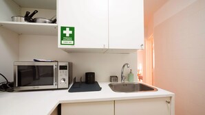 A kitchenette with a microwave, sink, and a first aid sign. - Nomad's Castel Lisbon - 1-Bedroom "The Traveler" (Lisboa ciudad)