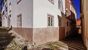A narrow cobblestone street flanked by buildings with large windows and a visible door. - Nomad's Castel Lisbon - 1-Bedroom "The Traveler" (Lisboa ciudad)