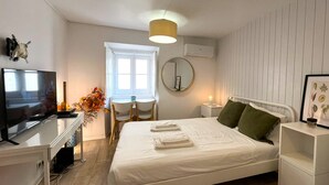 A bedroom with a bed, a desk with a TV, a window, and a bedside table with a lamp. - Nomad's Castel Lisbon - 1-Bedroom "The Traveler" (Lisboa ciudad)
