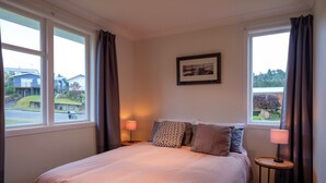 A bedroom with a large bed, two bedside lamps, a framed picture on the wall, and a view of the outside through the windows. - Poppa's Place: Safe & secluded, close to Lake Taupo & Tongariro (Omori)