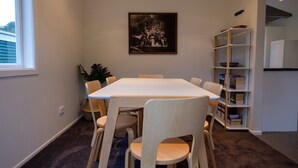 A dining area with a white table and chairs, a bookshelf, and a framed picture on the wall. - Poppa's Place: Safe & secluded, close to Lake Taupo & Tongariro (Omori)