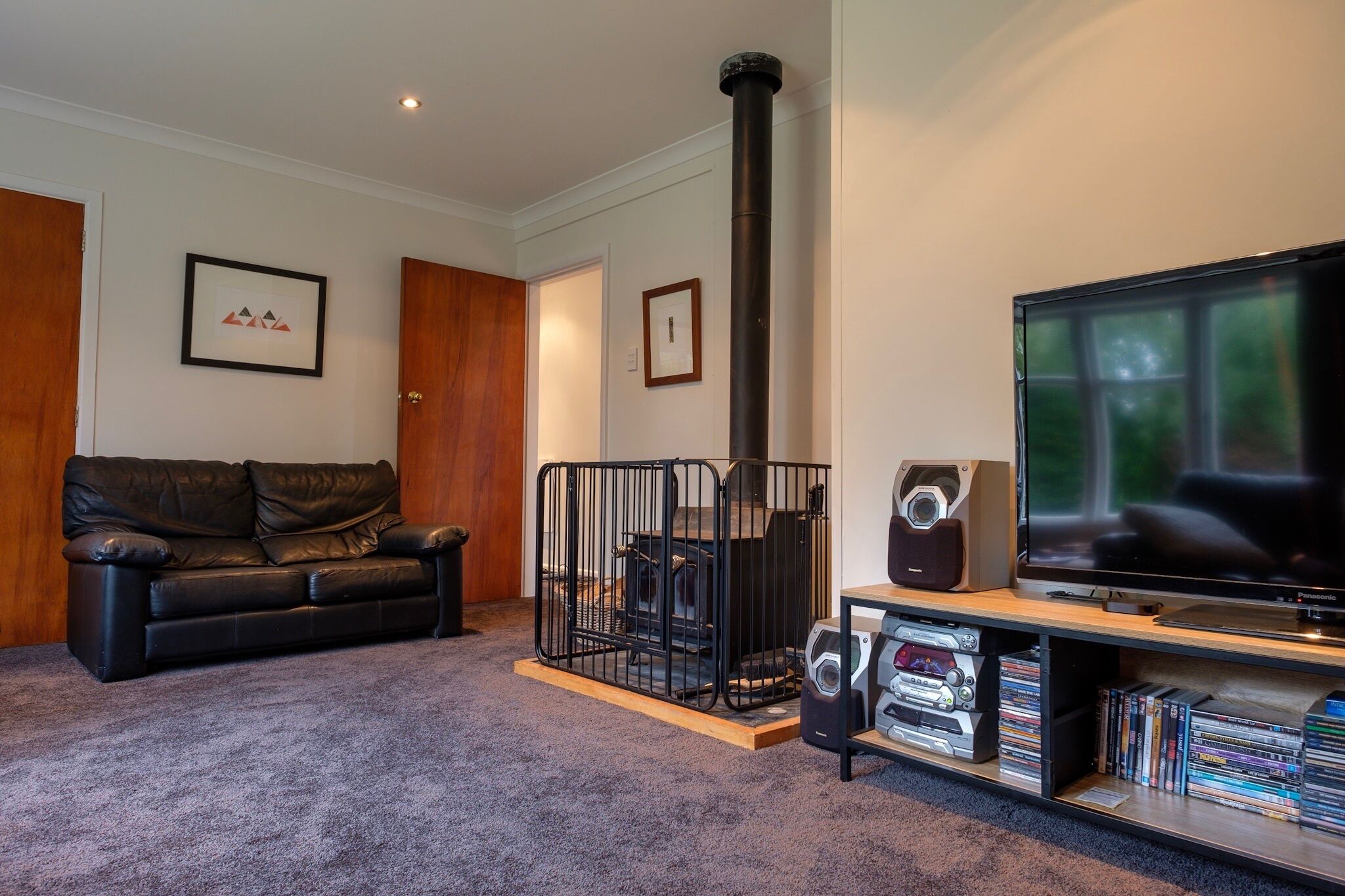 A living room with a black leather sofa, a fireplace, a television, and a bookshelf with DVDs.