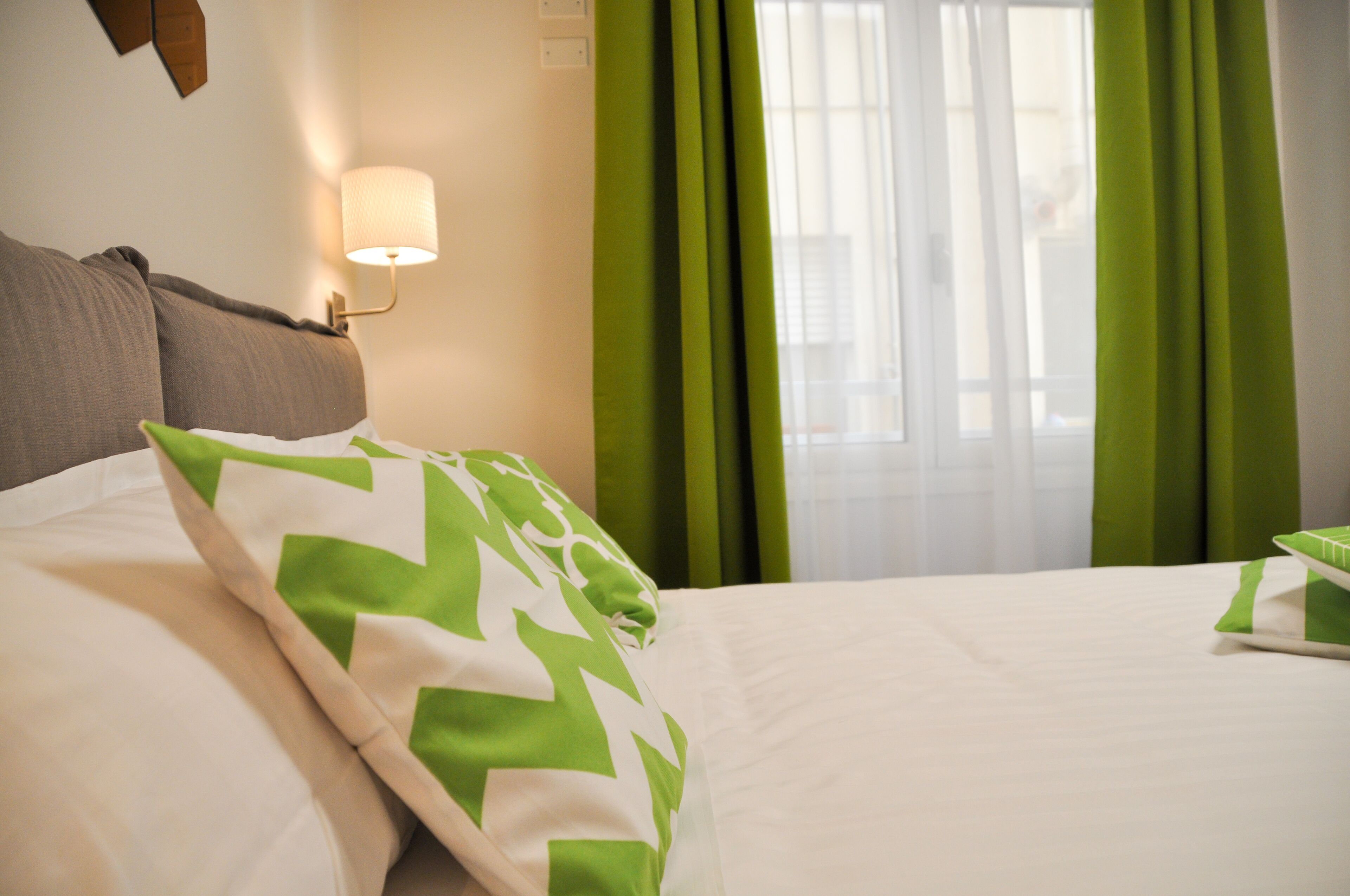 A hotel room with a bed, green curtains, and a wall-mounted lamp.