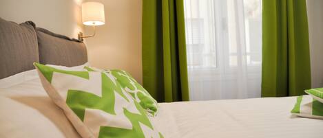 A hotel room with a bed, green curtains, and a wall-mounted lamp.