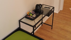Una habitación con una televisión de pantalla plana en la pared, una mesita con cafetera y una silla verde.