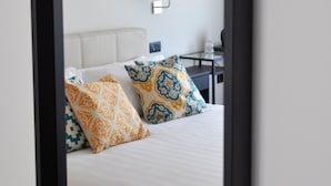 Una habitación de hotel con cama, almohadas, mesita de noche y lámpara.