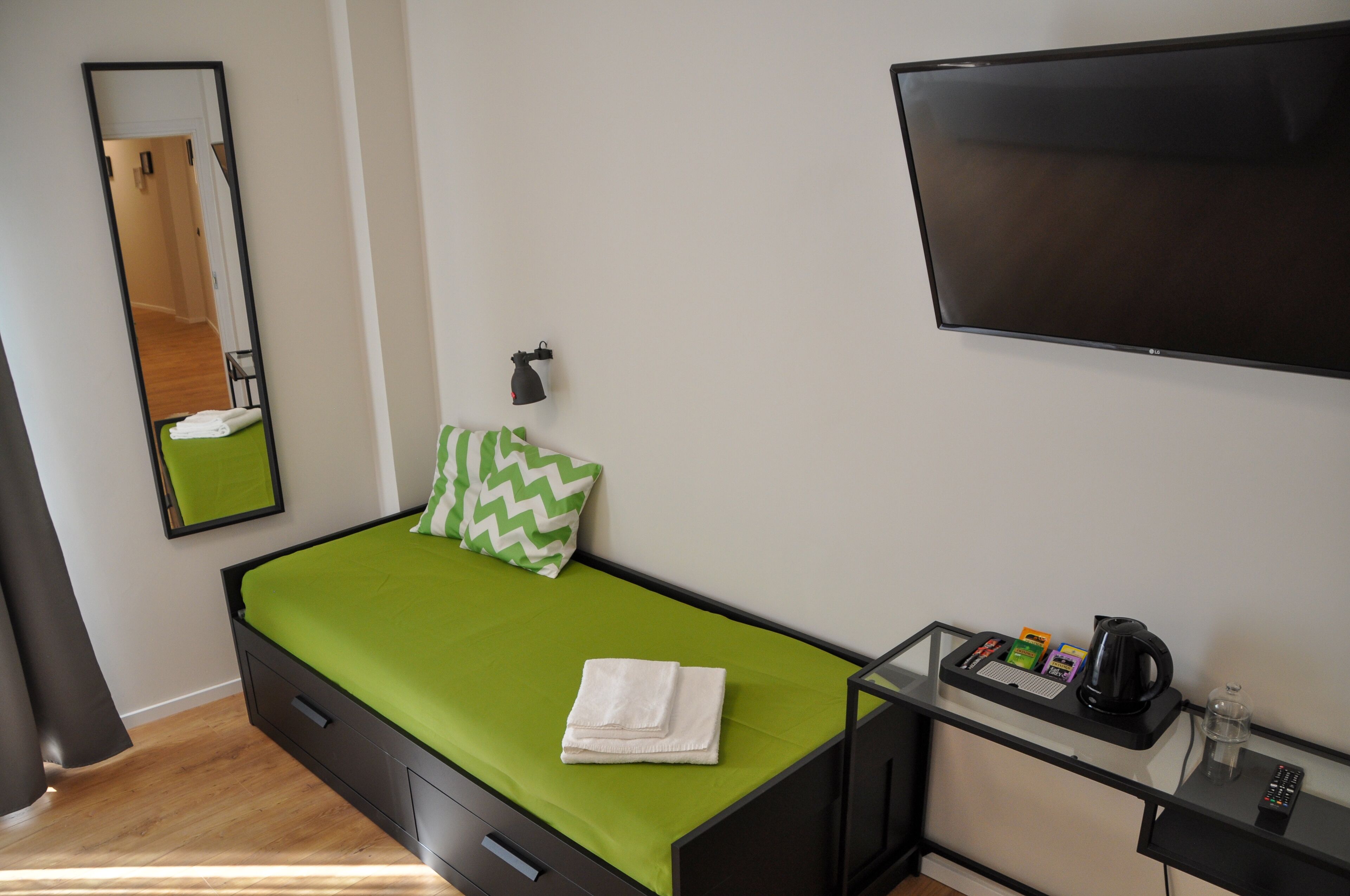 Une petite chambre moderne équipée d’un lit, d’une télévision, d’un miroir et d’un bureau avec une machine à café et une télécommande.