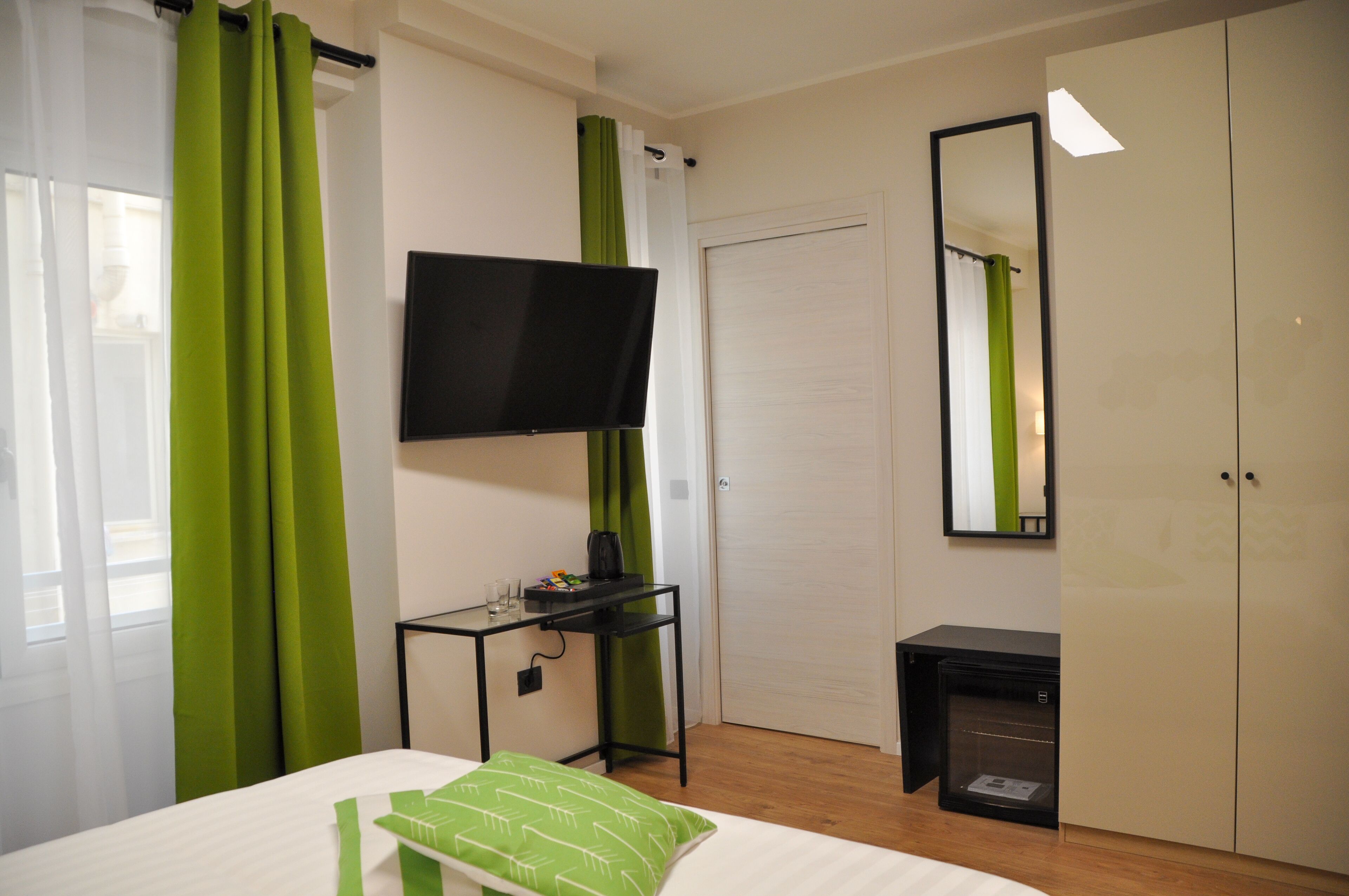 Habitación de hotel con cama, televisión montada en la pared, una mesita con tetera y armario.
