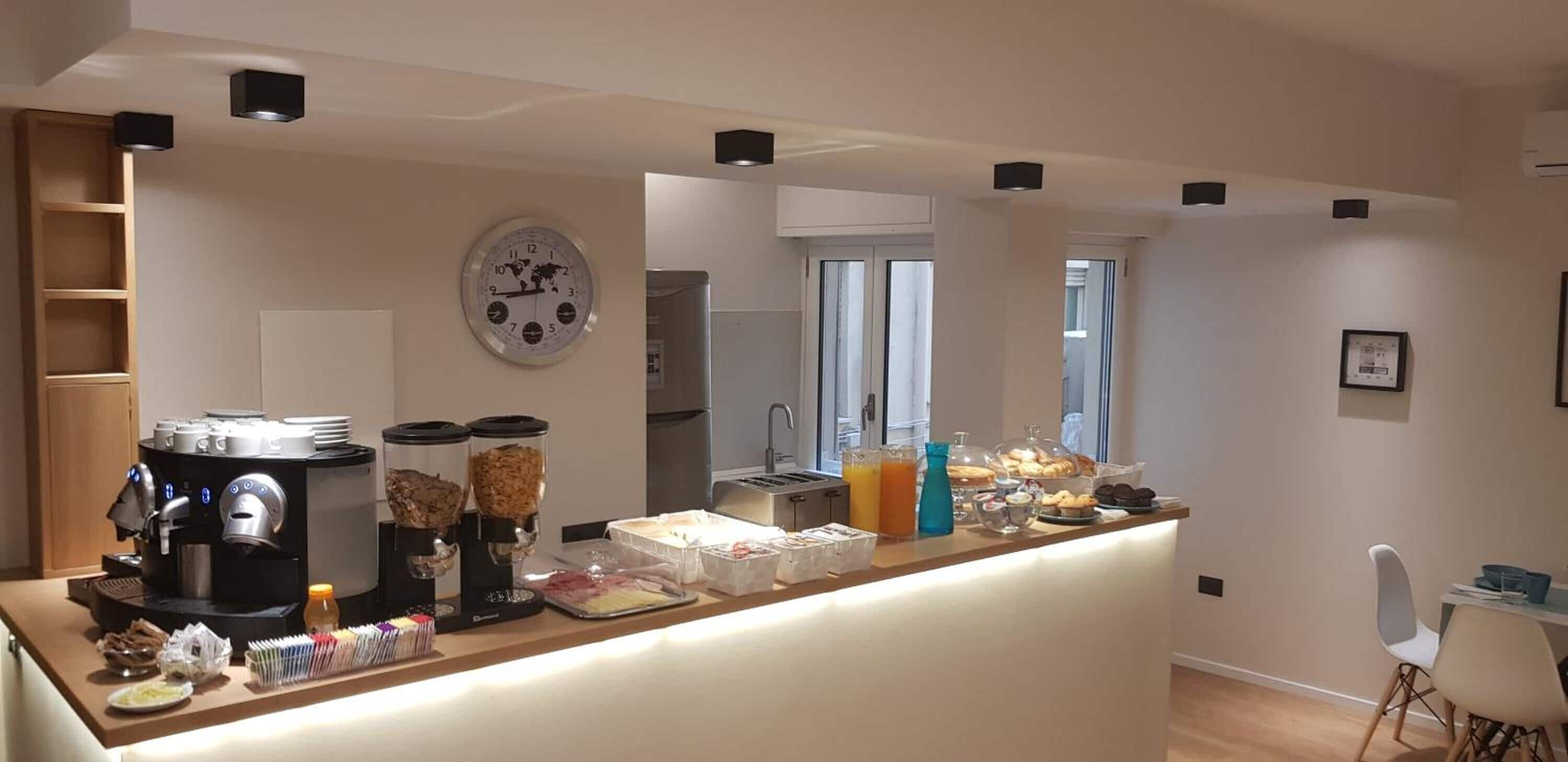 A modern kitchen with a coffee station, a clock, and a breakfast bar with various food items.