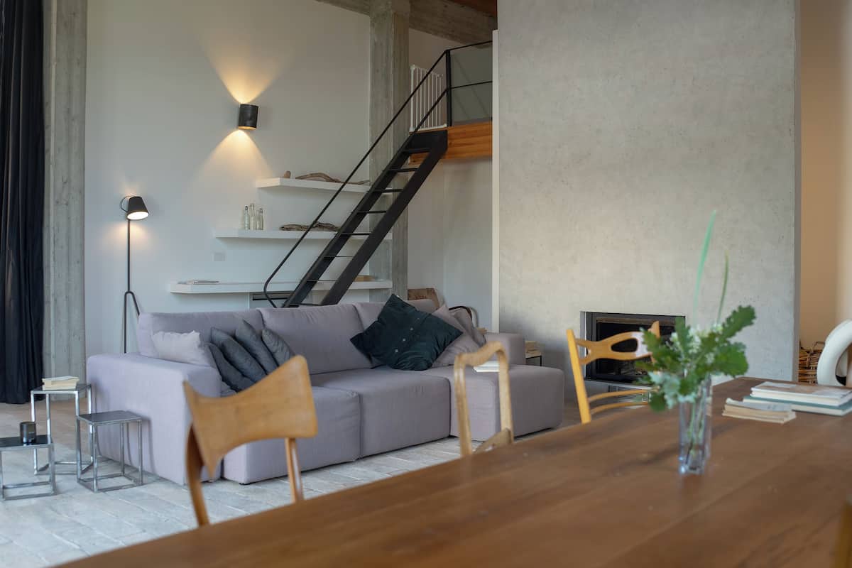 A modern living room with a sofa, wooden chairs, a dining table, and a staircase.
