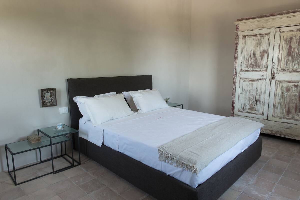 A bed with white linens, a dark headboard, and a bedside table with a glass top.