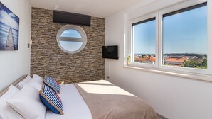 A bedroom with a stone wall, a round window, a bed with striped pillows, and a TV. - Villa Cindric (Medulin)