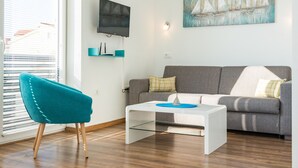 A modern living room with a grey sofa, a teal armchair, a white coffee table, a flat-screen TV mounted on the wall, and a painting of sailboats. - Villa Cindric (Medulin)