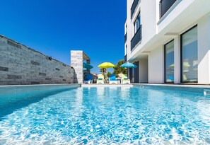 A swimming pool with clear blue water, surrounded by a stone wall and modern buildings. - Villa Cindric (Medulin)