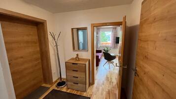 Een gang met houten deuren, een vloerlamp, een klein houten kastje en een spiegel aan de muur.