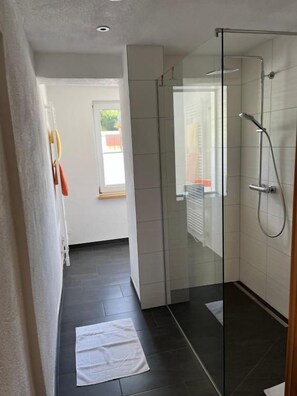 A modern bathroom with a glass shower enclosure, a white towel on the floor, and a window providing natural light. - Appartements-Restaurant Schwaiger (Bad Mitterndorf)
