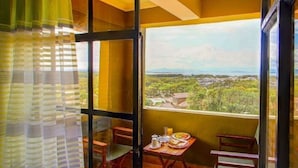 A balcony with a table set for breakfast, a chair, and a view of a landscape with trees and buildings. - Olive Resort (Naivasha)