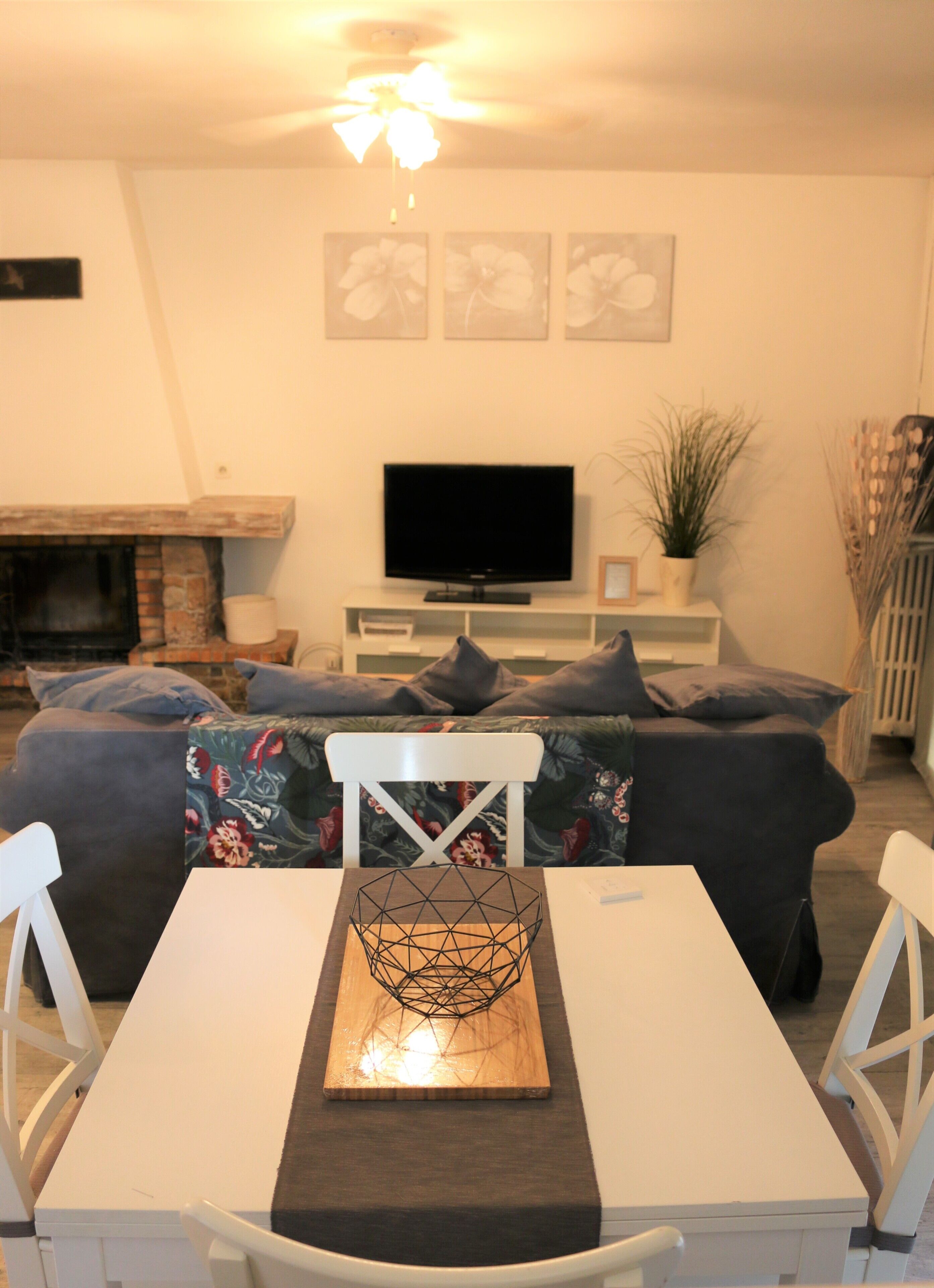 Una sala de estar con chimenea, un televisor de pantalla plana, una mesa de comedor con sillas y un sofá con cojines estampados.