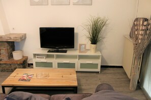 A living room with a flat-screen TV on a white cabinet, a coffee table with a magazine, a potted plant, and a fireplace.