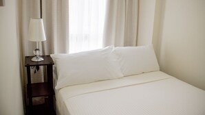 Cama bem arrumada com lençóis brancos em um quarto de hotel.