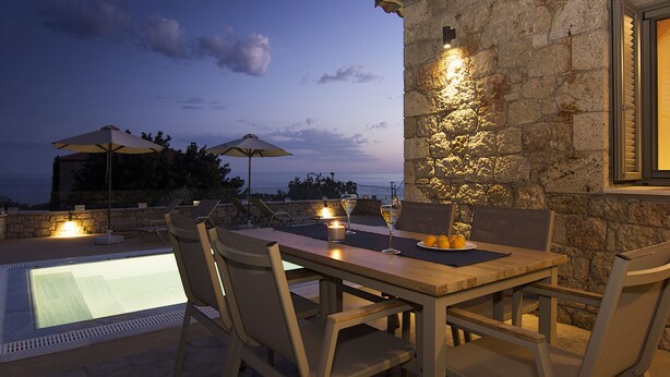 Un espace extérieur aménagé pour les repas, avec une piscine, des murs en pierre et des parasols.