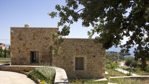 Un bâtiment en pierre, doté d’une petite porte et d’une fenêtre, entouré de verdure et surplombé d’un ciel dégagé.