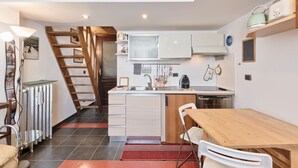 Une cuisine compacte dotée d’un îlot central, un coin repas avec une table et des chaises en bois, et un escalier menant à un niveau supérieur.