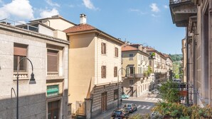 Une rue étroite bordée de bâtiments des deux côtés, un ciel dégagé et un balcon orné de plantes en pot.
