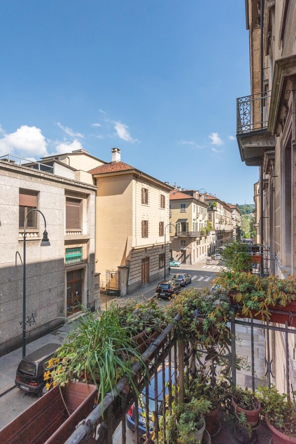 A narrow street with buildings on either side, a clear sky, and a balcony with potted plants. - Mole Antonelliana Lovely Loft (Turin)