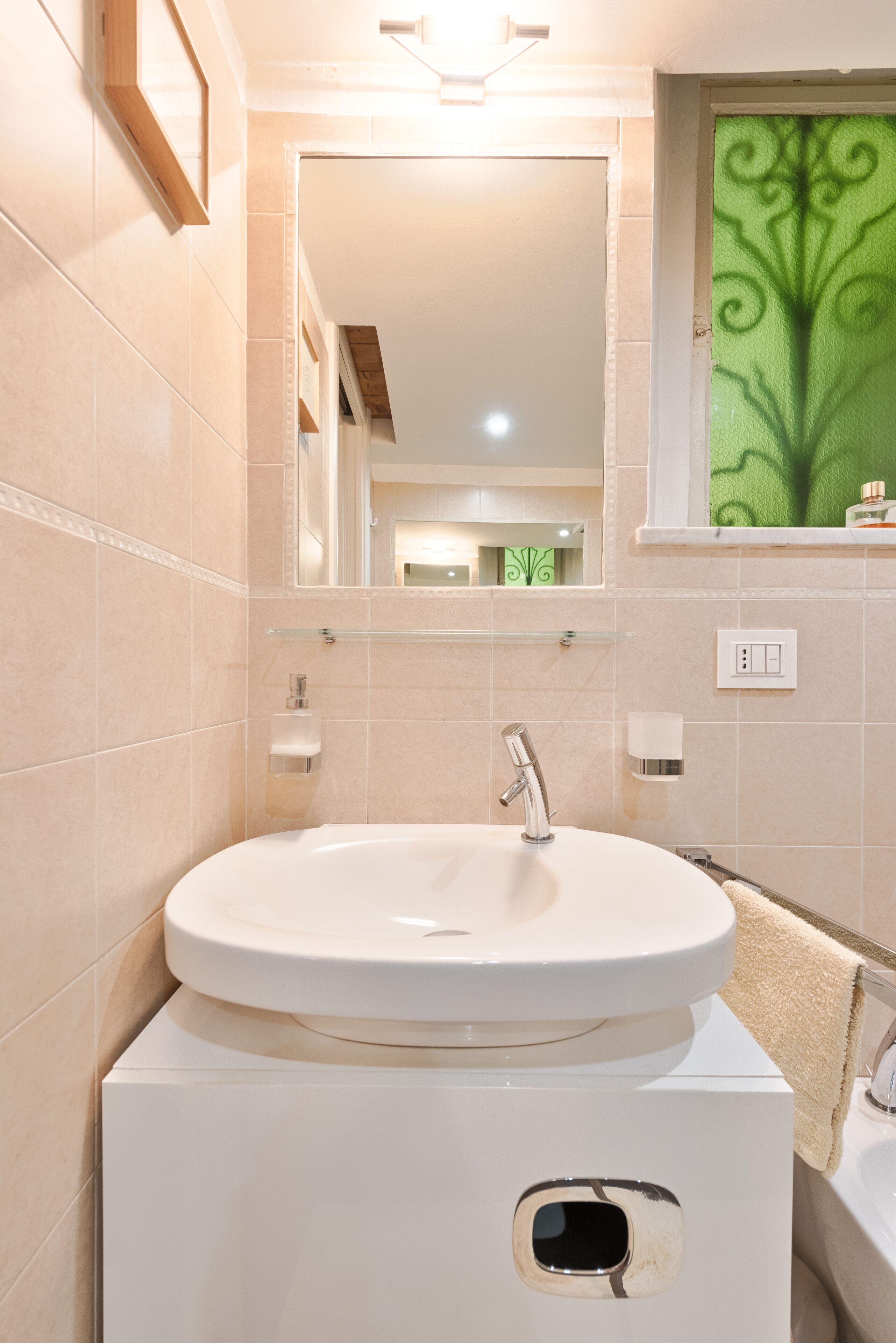 A bathroom with a white sink, a mirror, and a green decorative window.