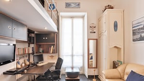 Un espace de vie compact comprenant un bureau, un ordinateur et une bibliothèque. On peut également apercevoir un canapé et un miroir.