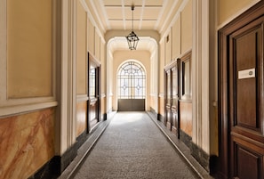 A hallway with marble walls, wooden doors, and a large arched window at the end. - Mole Antonelliana Lovely Loft (Turin)