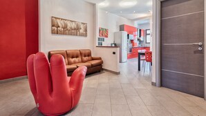 Ein modernes Interieur mit einem braunen Ledersofa, einem roten Sessel, einer Küchenzeile mit roten Stühlen und einer grauen Tür.