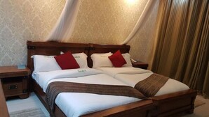 A double bed with white linens and red pillows, a wooden headboard, and a bedside table with a lamp. - Taidys Suites Kericho (Kericho)