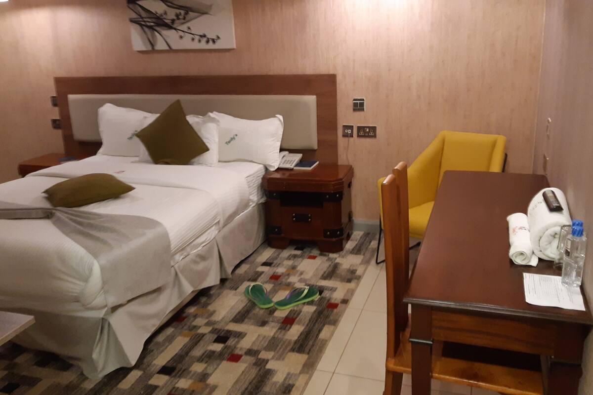 Una habitación de hotel con cama, mesita de noche, una mesa de madera con una silla y una alfombra pequeña.