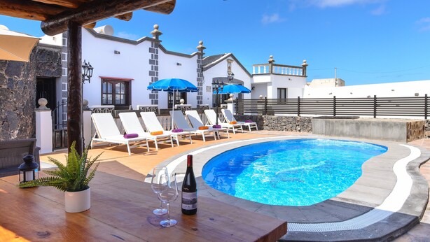 A poolside area with lounge chairs, a table with a bottle of wine, and a potted plant. - Spacious Villa "Las Calderetas" with Mountain View, Wi-Fi, Terrace & Pool (Mancha Blanca, Tinajo)