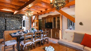 A dining area with a stone wall, wooden furniture, and a television in the background. - Spacious Villa "Las Calderetas" with Mountain View, Wi-Fi, Terrace & Pool (Mancha Blanca, Tinajo)