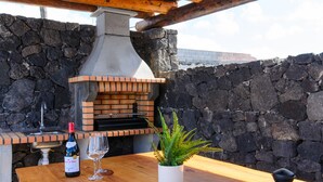 An outdoor patio with a stone wall, a brick oven, a bottle of wine, a glass, and a potted plant. - Spacious Villa "Las Calderetas" with Mountain View, Wi-Fi, Terrace & Pool (Mancha Blanca, Tinajo)